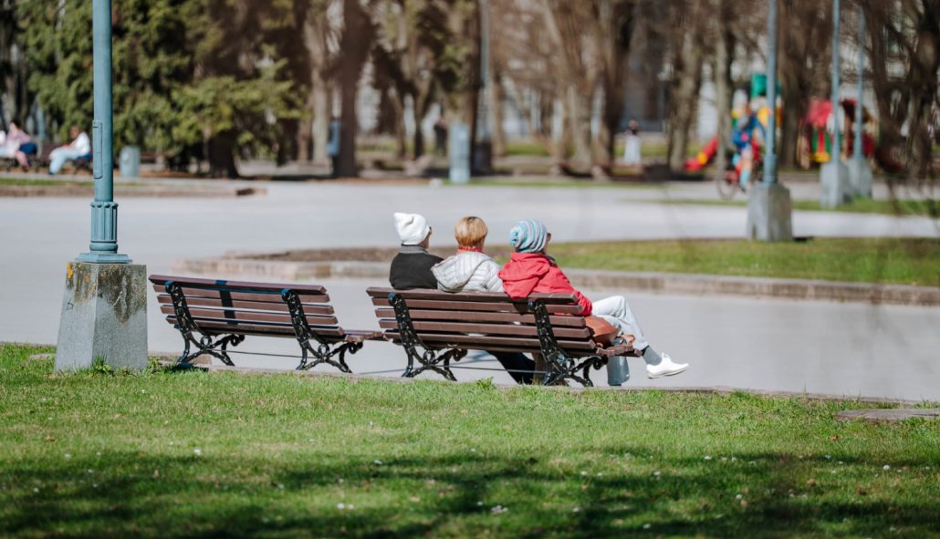 Foto: Cilvēki sēž uz soliņiem parkā, pavasaris