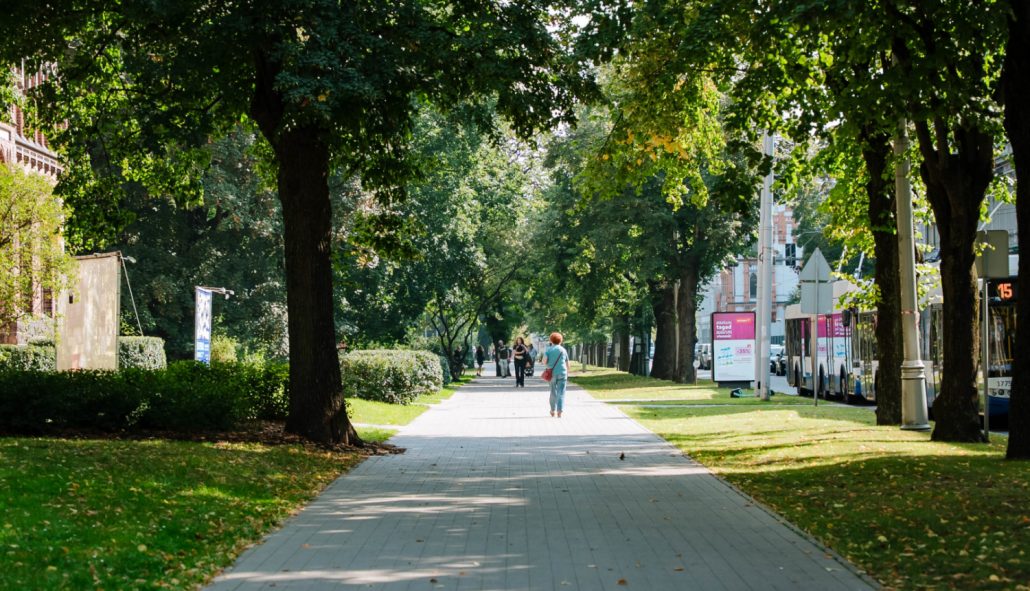 Cilvēki iet pa ielu, kamēr skolēni Rīgas centrā piedalās projektā “Elpo, Rīga!”, nēsājot sensorus gaisa kvalitātes mērīšanai