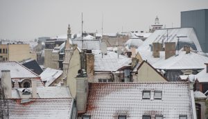 Dzīvojamā ēka Rīgā atkušņa laikā, uz jumta redzams kūstošs sniegs un lāstekas, uzsverot nepieciešamību regulāri tīrīt jumtu un uzturēt notekcaurules, lai novērstu bīstamas situācijas gājējiem un autovadītājiem.