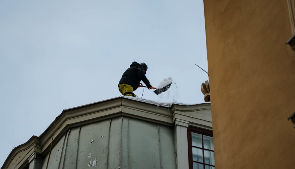 Namīpašnieks attīra sniegotu Rīgas ēkas jumtu, novēršot sniega un lāsteku krišanas riskus un nodrošinot gājēju drošību ziemas apstākļos.
