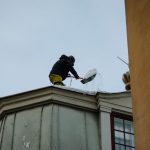 Namīpašnieks attīra sniegotu Rīgas ēkas jumtu, novēršot sniega un lāsteku krišanas riskus un nodrošinot gājēju drošību ziemas apstākļos.