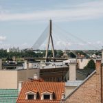 Skats uz Rīgas pilsētvidi ar Vansu tiltu un ēku jumtiem, ilustrējot tēmu “Rīga gaiss kvalitāte programma” un saistītos gaisa kvalitātes uzlabošanas pasākumus.