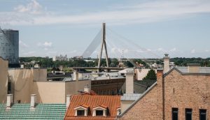 Skats uz Rīgas pilsētvidi ar Vansu tiltu un ēku jumtiem, ilustrējot tēmu “Rīga gaiss kvalitāte programma” un saistītos gaisa kvalitātes uzlabošanas pasākumus.