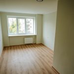 Atjaunots sociālais dzīvoklis Rīgā ar gaišām sienām, lamināta grīdu, logu un radiatoru istabas galā. Attēlā redzama dzīvošanai sagatavota telpa pēc remonta. Rīgas sociālo mājokļu atjaunošana nodrošina kvalitatīvu dzīves vidi iedzīvotājiem.