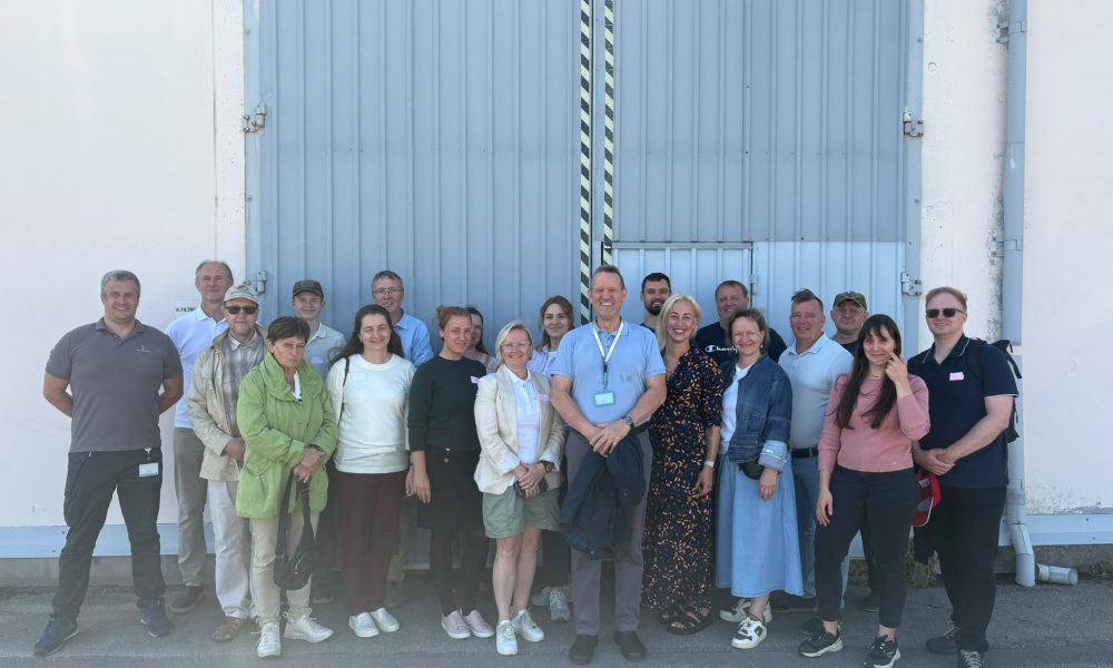 RE-FRESH projekta partneri un eksperti tehniskās vizītes laikā, iepazīstoties ar ūdens attīrīšanas procesu risinājumiem projekta aktivitāšu ietvaros. RE-FRESH projekta partneri un eksperti grupas fotoattēlā pie industriālas ēkas. Attēlā redzama projekta dalībnieku grupa āra teritorijā pēc tehniskās vizītes, kas veltīta ūdens attīrīšanas procesu un ezeru atjaunošanas risinājumu izpētei. RE-FRESH ezeru atjaunošanas projekts veicina pārrobežu sadarbību ūdens kvalitātes uzlabošanai.